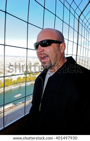 Bald man bored and yawning up high on top of a tower in Paris.