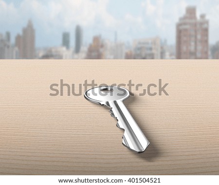 Silver key on wooden table, with cityscape background.