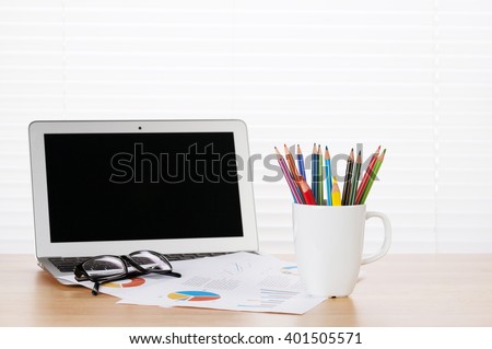 Office workplace with laptop, reports and pencils on wooden desk table in front of window with blinds