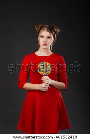 Portrait of a smiling young beautiful girl in a red dress with a big candy. Funny girl with a lollipop