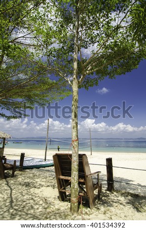 wooden chair under a tree facing the clear blue sea water at sunny day.cloudy white cloud and blue sky background. white sandy tropical beach