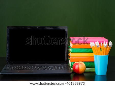 Laptop and pile of books near empty green chalkboard. Sample for text