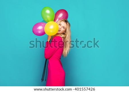 beautiful blonde woman very energetic, smiling and holding some colored balloons on blue background