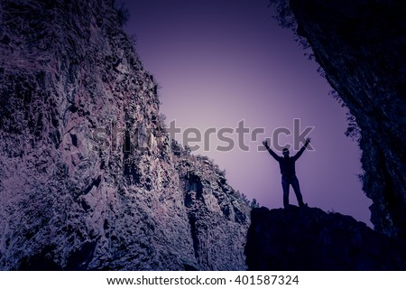 Silhouette of a man standing on a rock near the cave against the sky
