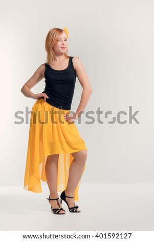 Beautiful young blonde girl in a black top, a yellow skirt and black high heel shoes dancing