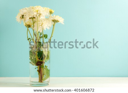 selective focus chrysanthemum flower,water in glass.Glass on the white,green table wood  background.