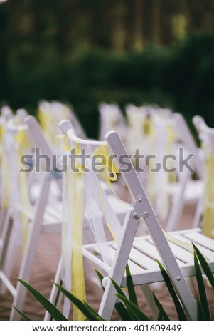 White chairs decorated with yellow cloth waving in the wind on the wedding ceremony
