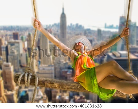 Happy, young and attractive woman with colorful sarongs and white wide-brimmed hat swinging on the New York city background defocused. Freedom concept