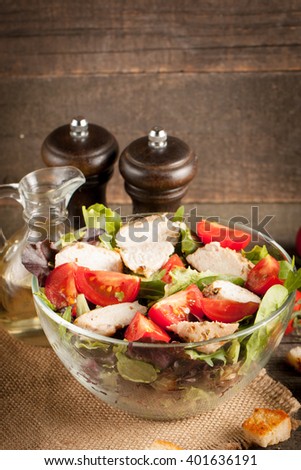 Fresh salad made of tomato, ruccola, chicken breast, arugula, crackers and spices. Caesar salad in a white, transparent bowl on wooden background