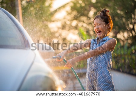 Happy Asian girl washing car on water splashing and sunlight at home Royalty-Free Stock Photo #401667970