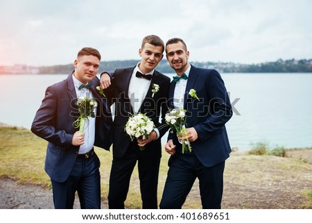 Confident smiling handsome groom in black suit with two groomsman  Royalty-Free Stock Photo #401689651