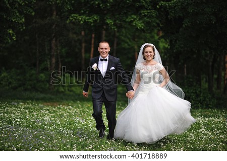 Happy newlyweds running at field of white flowers