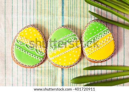 Easter homemade gingerbread cookie and yellow end green eggs over grenn and white cloth. Colorful image, top view