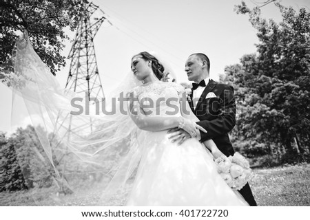 Fashionable wedding couple background electrical tower, long veil of bride. B&W photo