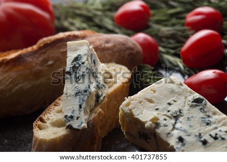 Blue cheese with french baguette, tomato and herbs on black marble table. Traditional snacks in France and Italy closeup.