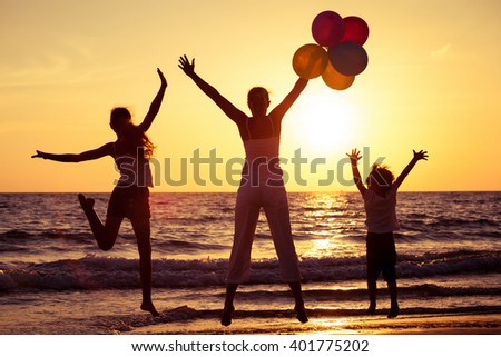 Mother and children playing with balloons on the beach at the sunset time. Concept of friendly family.