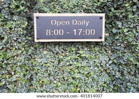Iron plate and wooden open sign on green tree wall.