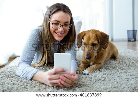 Portrait of beautiful young woman with her dog using mobile phone at home. Royalty-Free Stock Photo #401837899