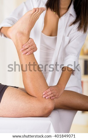 Female physio therapist hands working on male patients legs, holding and bending, blurry clinic background