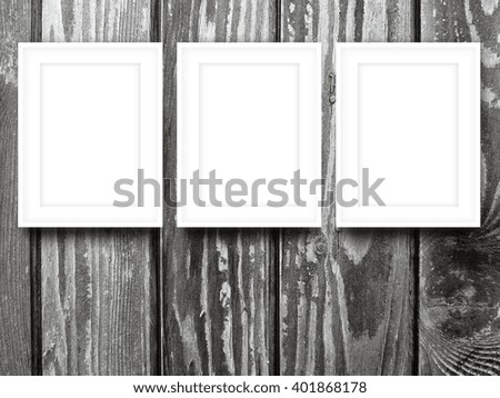 Close-up of three white blank picture frames on monochrome wooden background