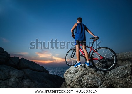 Man standing with a bicycle on the rock during sunset
