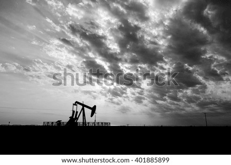 Cloudy sunset and silhouette of crude oil pump in oilfield - Black and white