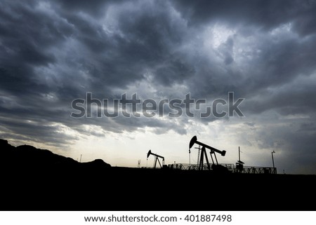 Cloudy sunset and silhouette of crude oil pump in oil field.