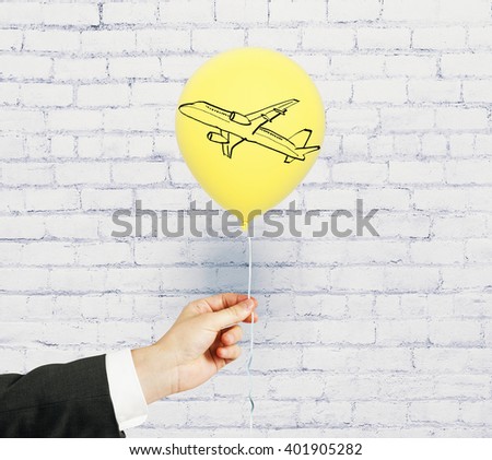 Hand holding a yellow balloon with plane drawing on white brick wall background