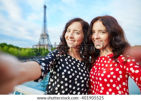 Beautiful twin sisters taking selfie in front of Eiffel Tower while traveling in Paris, France. Happy smiling girls enjoy their vacation in Europe