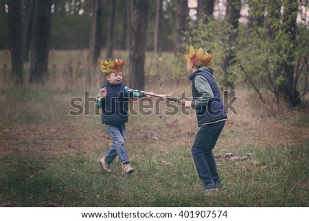 Two Brothers running in a forest on autumn day. Boys have a crown from leaves on the head and swords in hands