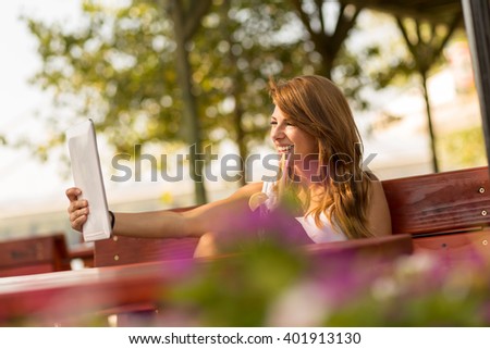 Beautiful brunette sitting in an outdoor cafe, taking a selfie with her tablet computer and drinking lemonade