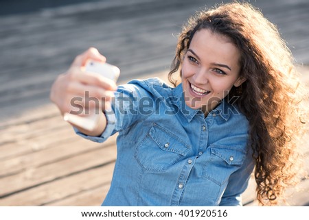 Beautiful smiling and happy young woman is taking selfie photo with smartphone outdoor.Instagram