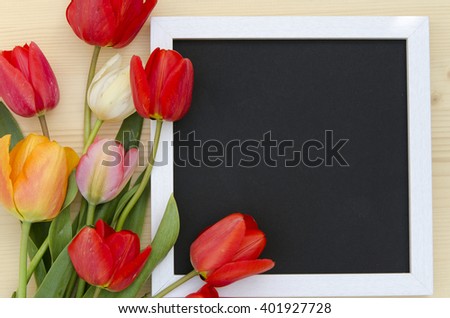 Tulips with blank black chalkboard picture frame on a light wooden background. romantic picture.  