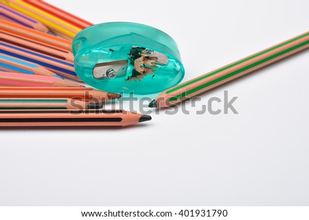 Picture of some pencils with stripes of different colors and green pencil sharpener with pencil shavings on it on a white background. Selective focus