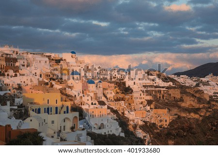 Image of white city on a slope of a hill at sunset and pink clouds, Oia, Santorini, Greece