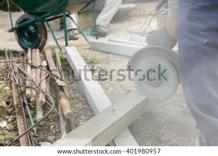 Construction worker cutting a reinforced concrete pillar for installation with coworker in the background resting. Construction business, DIY, dirty and dangerous work around the house concept. 
