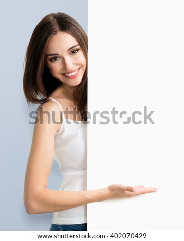Portrait of happy smiling young woman in white tank top casual smart clothing, showing empty blank signboard with copyspace area for text or slogan