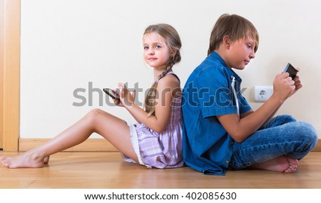Little girl and teenage boy burying in mobile phones sitting on the floor
 Royalty-Free Stock Photo #402085630