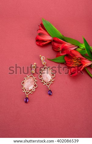 Jewelry earrings with topazes and diamonds next to lilies on pink background. 