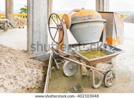 Old Cement mixer machine with sand truck stop beside at a construction site.