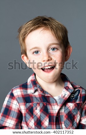 portrait of a young kid with freckles and blue eyes playing with his mouth for fun wellbeing, grey background studio