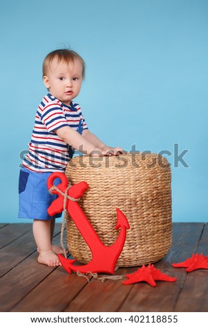 A boy in the marine dress standing on the wooden floor and blue background with a red anchor and red starfish