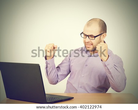 Funny photo of businessman bald with beard wearing shirt and glasses.  angry businessman working with laptop at table. Isolated on gray background 