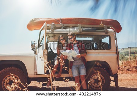 Young couple taking a break to look at a map while on a roadtrip. Young man and woman on country road looking for directions on map. Royalty-Free Stock Photo #402214876