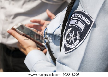 Israeli female police officer with an emblem on her uniform holding cellular phone in her hands. Israeli police concept, coronavirus restrictions fine issued. Tel Aviv, Israel, April 2014.  Royalty-Free Stock Photo #402218203