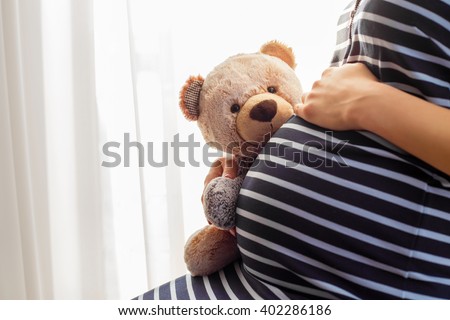 Pregnant woman sitting and holding teddy bear toy 