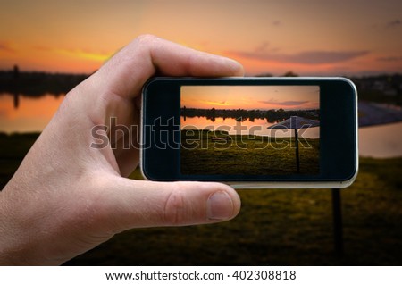 photo on the phone, the person photographed on a smartphone from the side. evening landscape, the setting sun on the beach. selfie