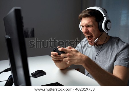technology, gaming, entertainment, play and people concept - angry screaming young man in headset with controller gamepad playing computer game at home and streaming playthrough or walkthrough video Royalty-Free Stock Photo #402319753