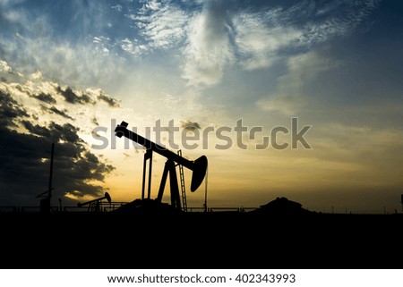 Cloudy sunset and silhouette of crude oil pumping unit in the oil field.
