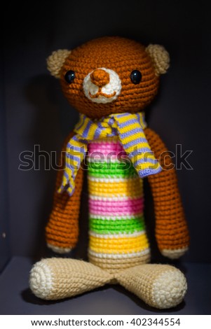The knit brown teddy bear tied a scarf and placed in a box. Hand made crochet doll